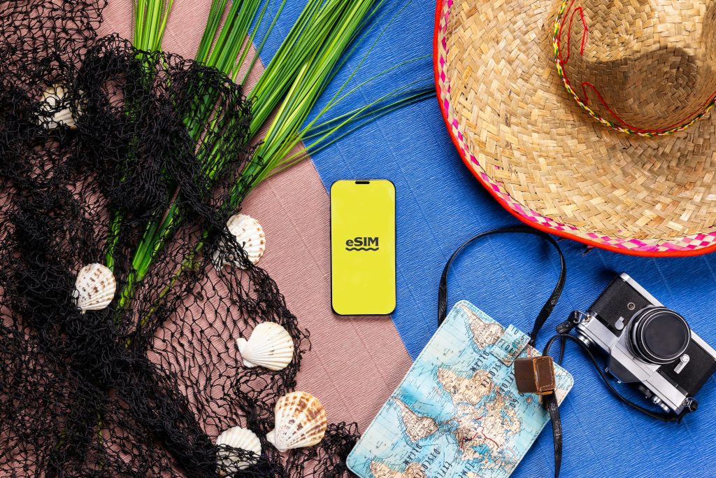 A vibrant flat lay of travel items featuring a smartphone with eSIM, hat, camera, and map.