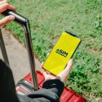 A person holds a smartphone showing an eSIM app while standing with luggage outdoors in Los Angeles.